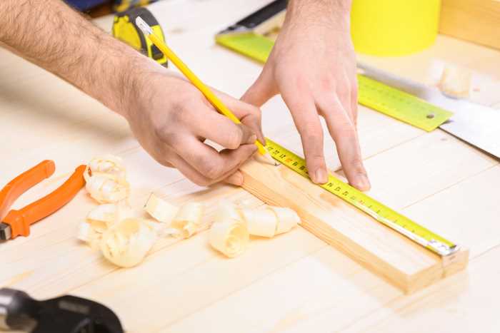 Shown is a person measuring a plank of wood before sawing.
