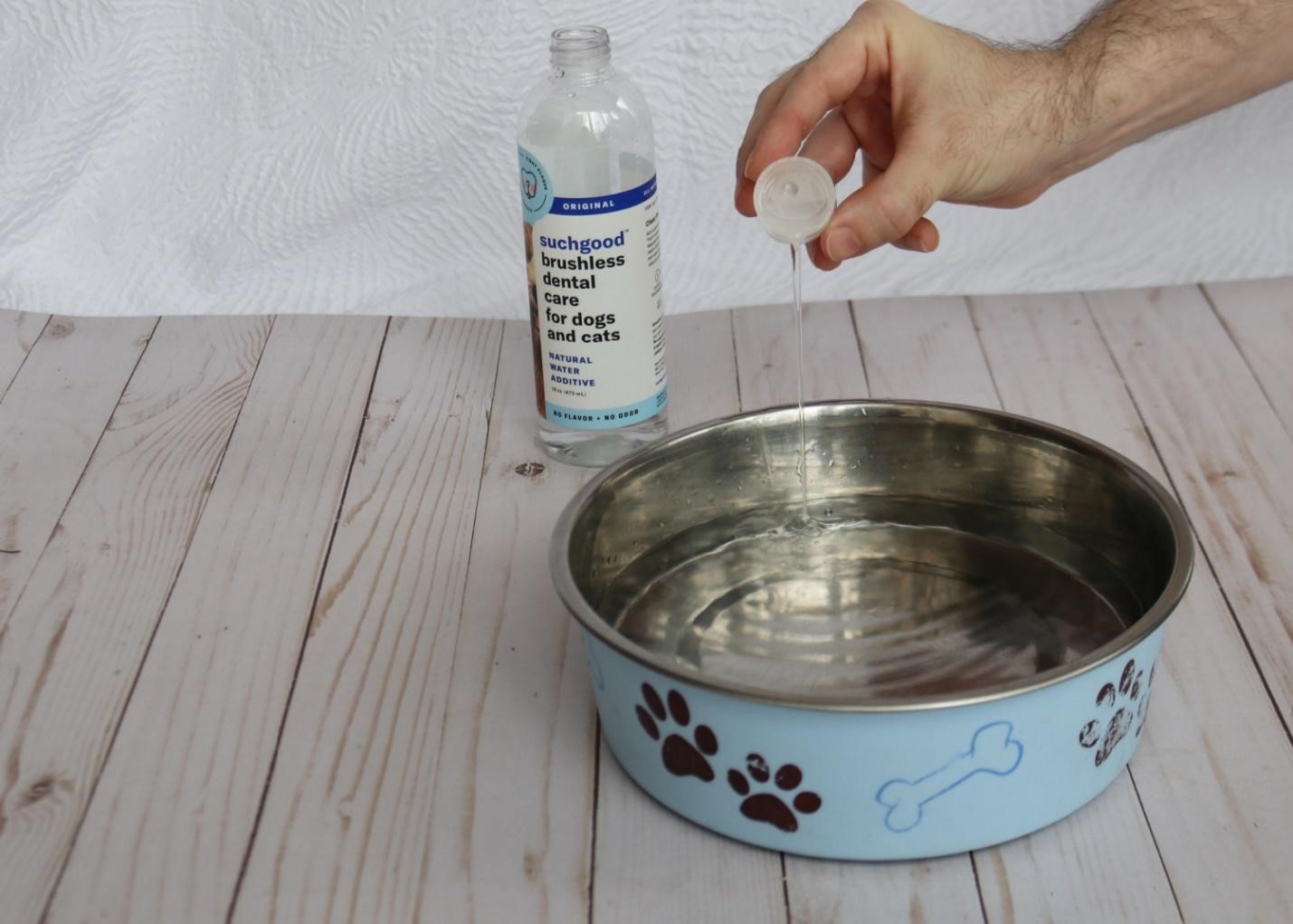 Shown are a bowl of dog water and Suchgood water additive