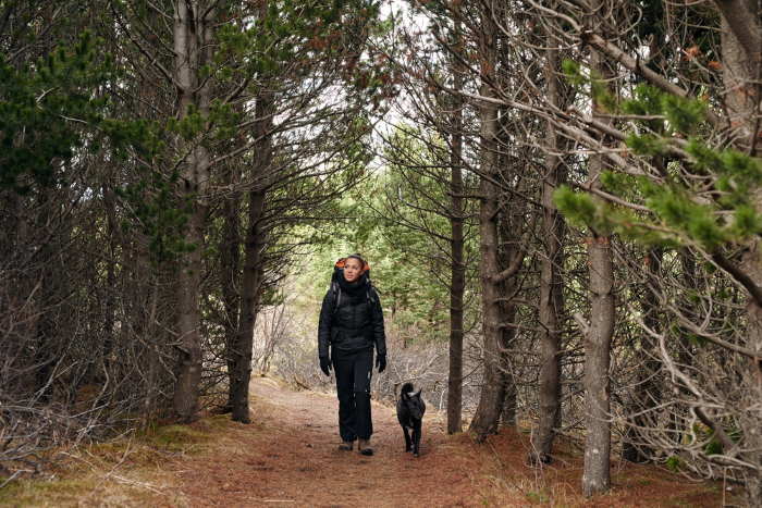a woman with a small dog is hiking along a trail.