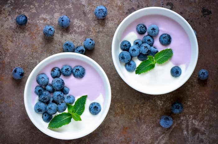 Two bowls of yogurt topped with fresh blueberries