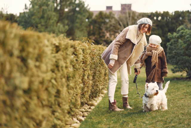 A mother and daughter are standing near their West Highland White Terrier. A mother and daughter are standing near their West Highland White Terrier.