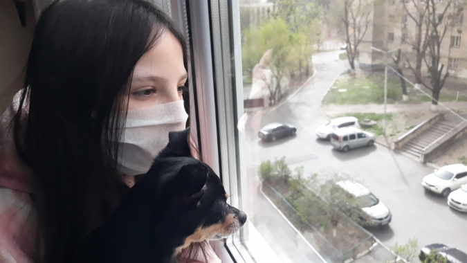 A girl wearing a mask is holding her small dog.