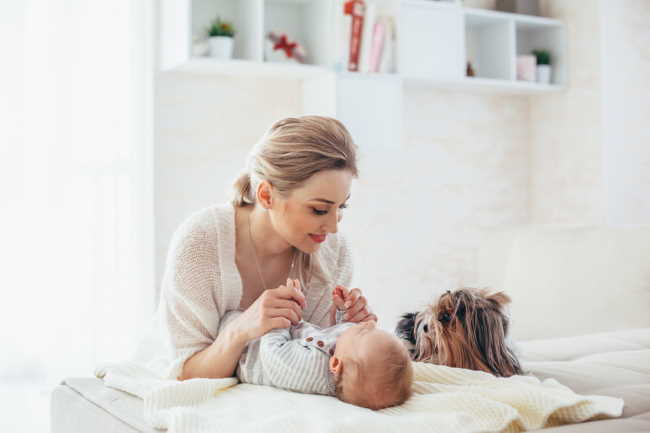 A mother is playing with her baby as a Yorkshire Terrier looks on.