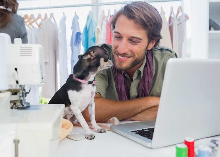 A girl is sitting at a desk writing while holding her dog on her lap.