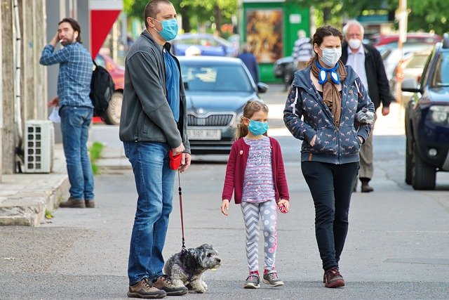 Parents and young child wearing masks is walking their small dog.