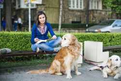 A young woman is sitting on a bench holding leashes to two large dogs with link to the article.