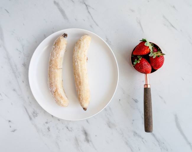 Frozen bananas and spoon of strawberries